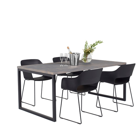 A modern dining table set for 4 with a dark wooden table, four black chairs with sleek frames, an ice bucket with champagne, two glasses, and a vase with green plants.