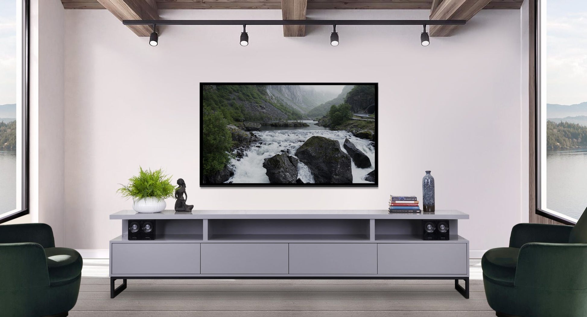 A modern living room with a large TV displaying a nature scene, flanked by green potted plants and books on a sleek white media stand, dark speakers, against a backdrop of serene lake views through