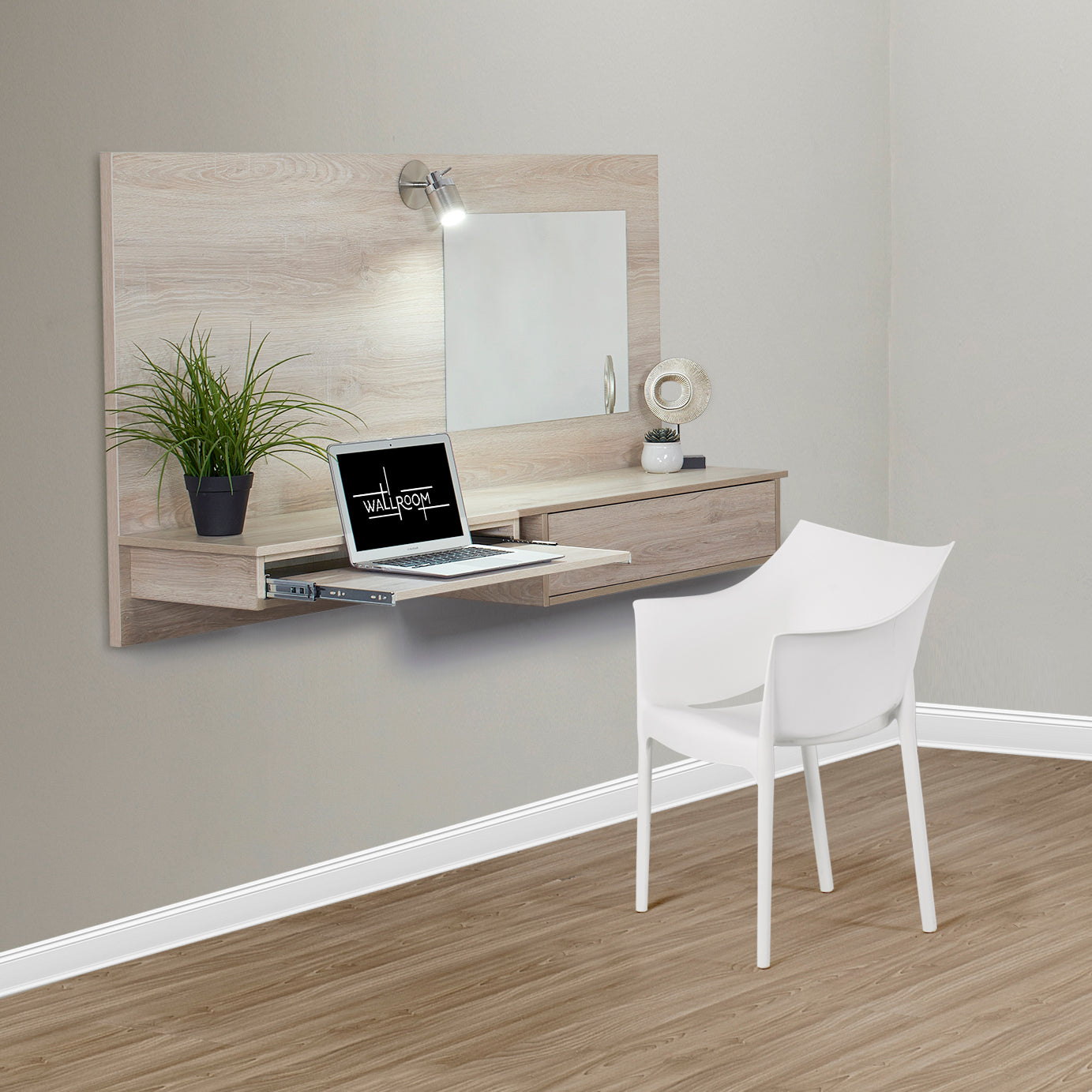 A minimalist home office setup with a sleek wooden floating dresser, white modern chair, laptop, decorative plants, and stationery, against a gray wall with a mounted lamp and mirror.